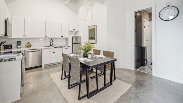 A modern kitchen with white cabinets, stainless steel appliances, and a dining area with a dark table and wicker chairs. - Centrally located, unique and brand new condo (Houston)