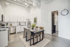 Una cocina moderna con armarios blancos, electrodomésticos de acero inoxidable y un comedor con una mesa oscura y sillas de mimbre.