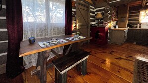 A rustic cabin interior with a wooden table, bench, and a fireplace.