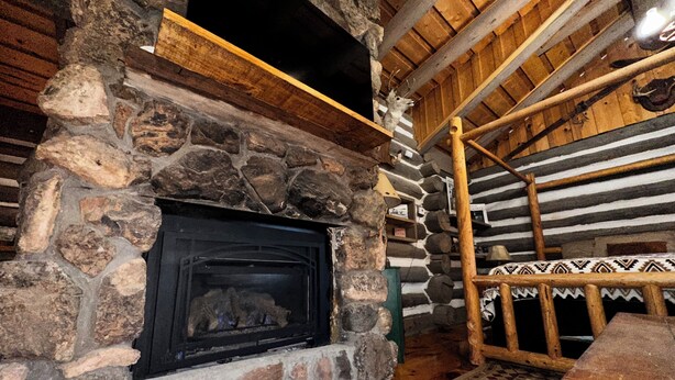 A stone fireplace with a wooden mantel, a checkered floor, and a wooden ceiling with beams.
