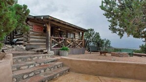 A rustic log cabin with a porch, stone steps, and a sign reading "Cowboy's Place."