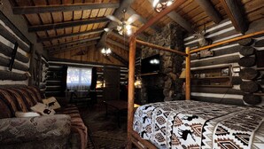 A log cabin interior with a four-poster bed, a stone fireplace, and a television mounted on the wall.