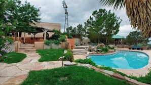 A backyard with a swimming pool, a pergola, and a windmill.