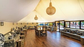 A spacious tented area with a dining table, chairs, sofas, and hanging light fixtures.