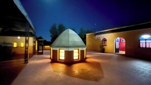Een binnenplaats met een verlichte constructie in het midden, mogelijk een pergola, omringd door gebouwen met gebogen ramen en deuren.