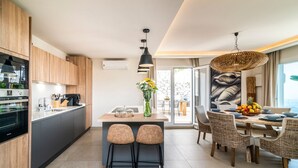 A modern kitchen with wooden cabinets, a built-in oven, and a dining area with wicker chairs and a fruit bowl.