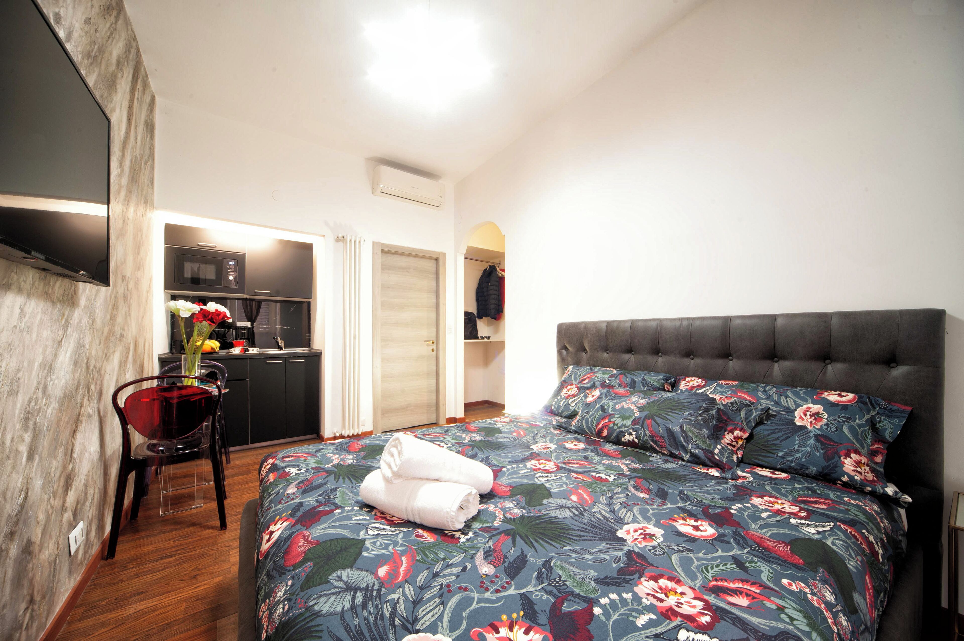 Un dormitorio con cama, una silla, un escritorio y una kitchenette.