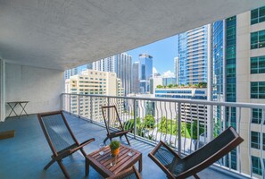 Een balkon met twee loungestoelen en een kleine tafel, met uitzicht op een stadsbeeld met moderne gebouwen.