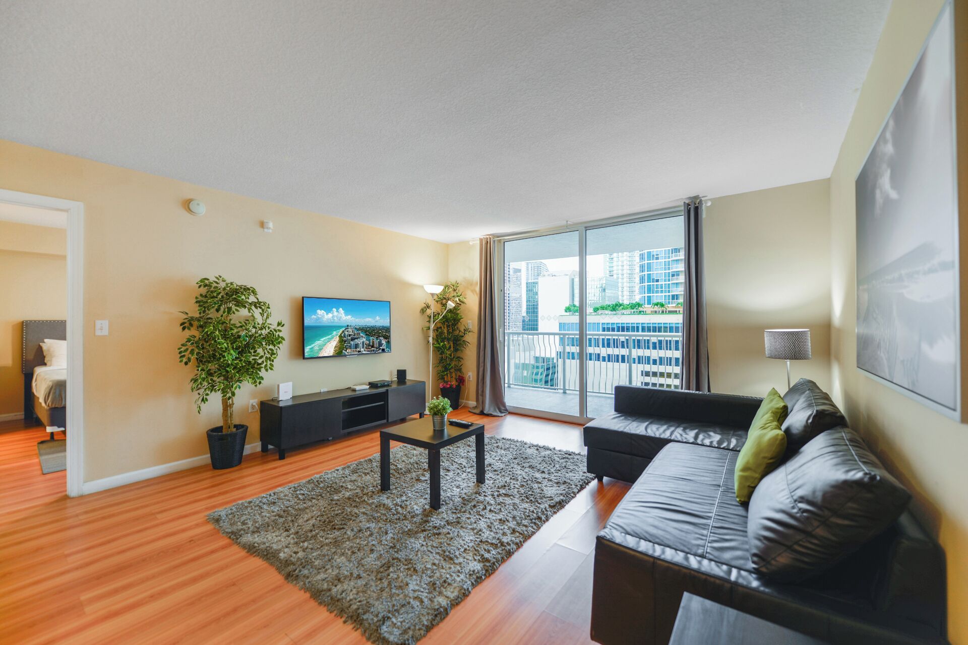Een moderne woonkamer met een bank, televisie en grote ramen met uitzicht op de stad.