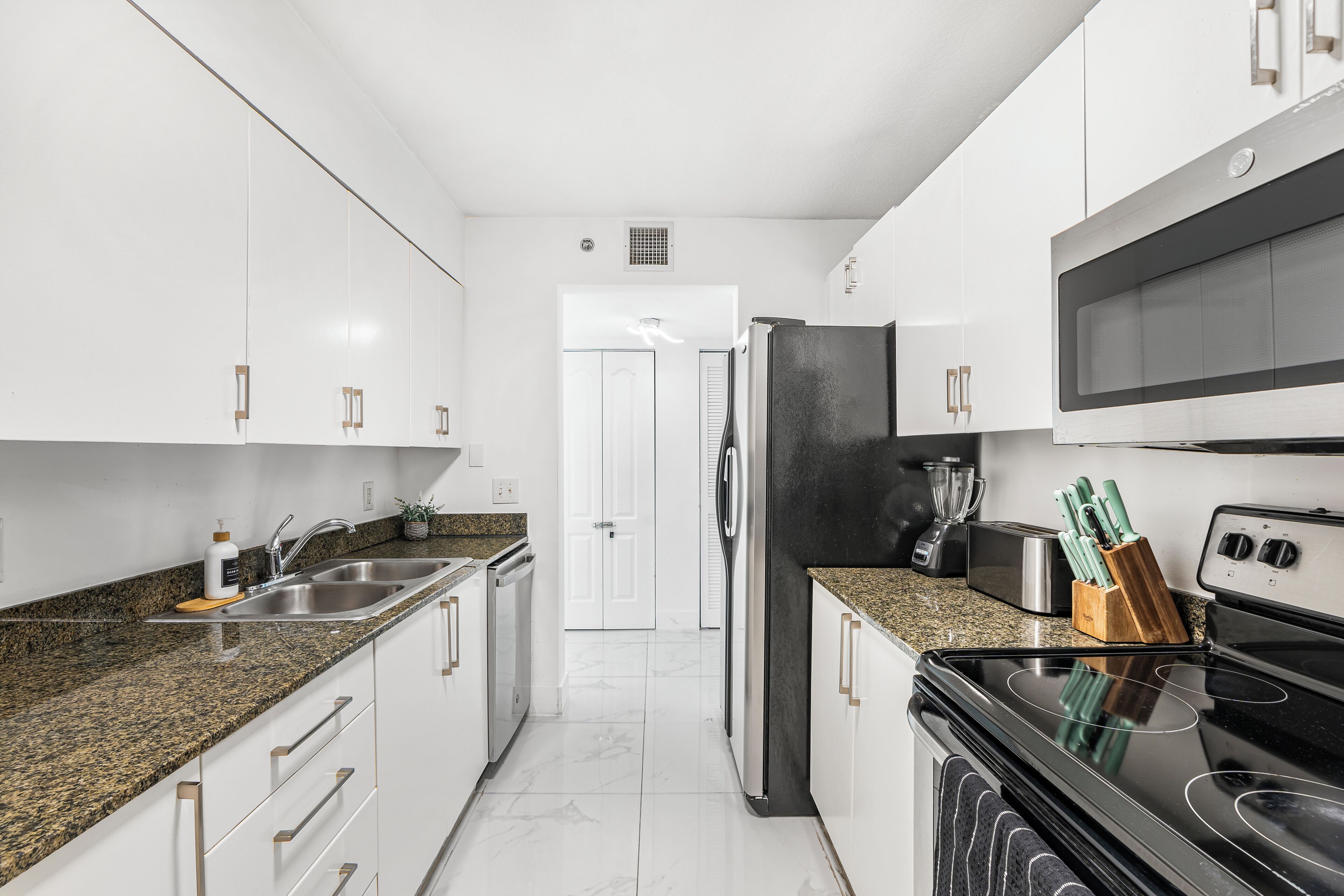A modern kitchen with white cabinets, granite countertops, stainless steel appliances, and a black refrigerator.