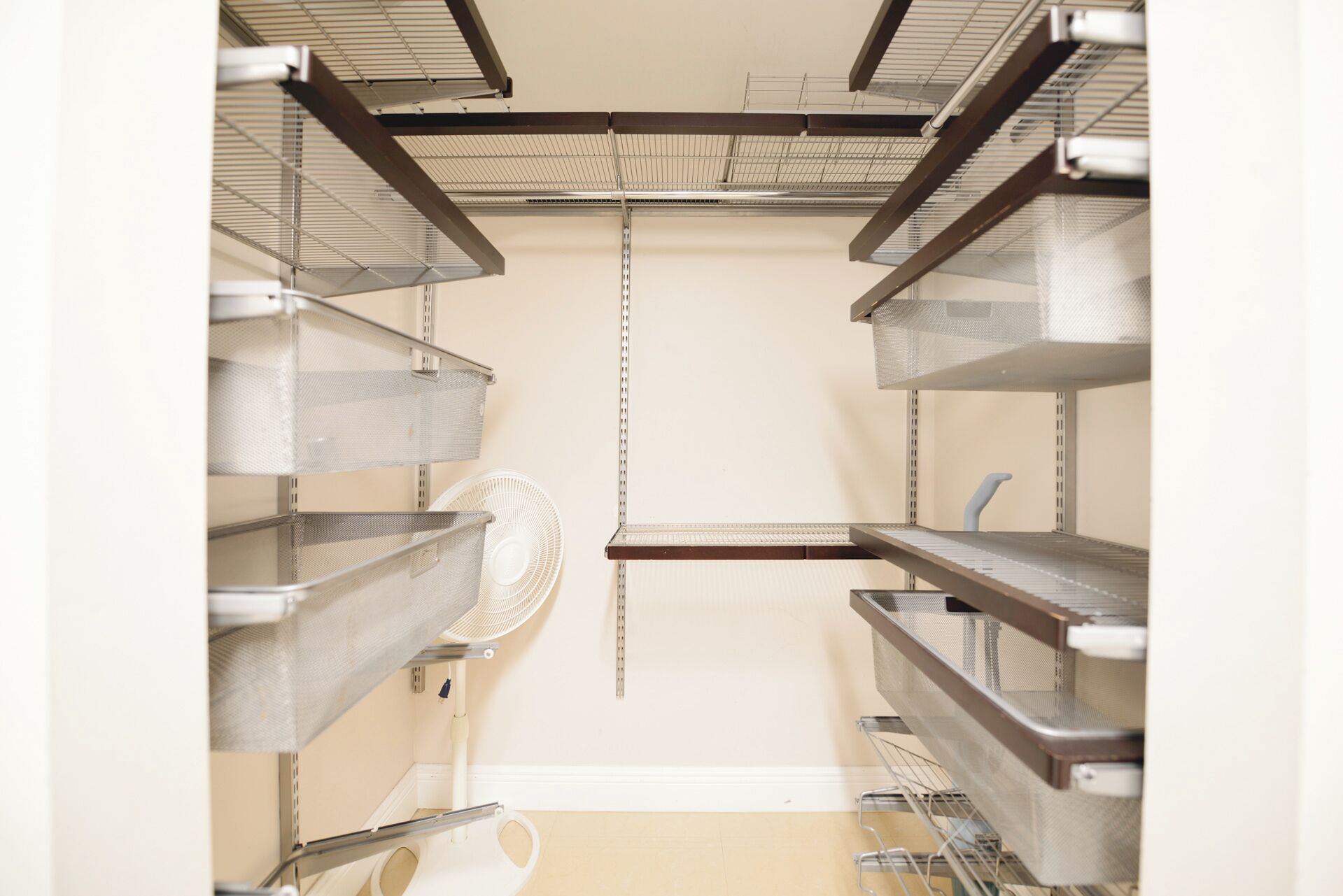 A storage closet with metal shelving units, a white fan, and a white toilet.