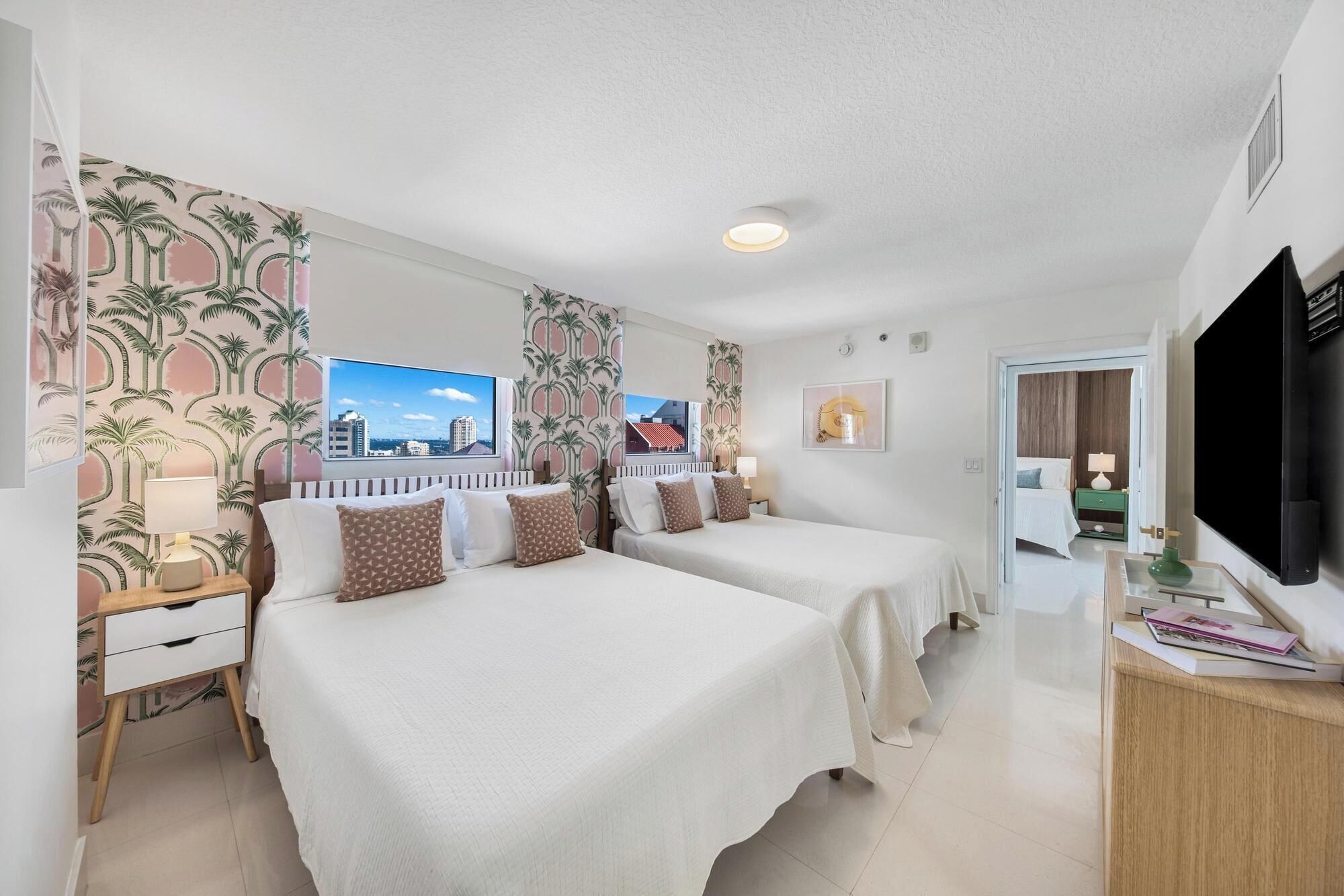 Habitación de hotel con dos camas, televisión, escritorio y ventana con vista a la ciudad.