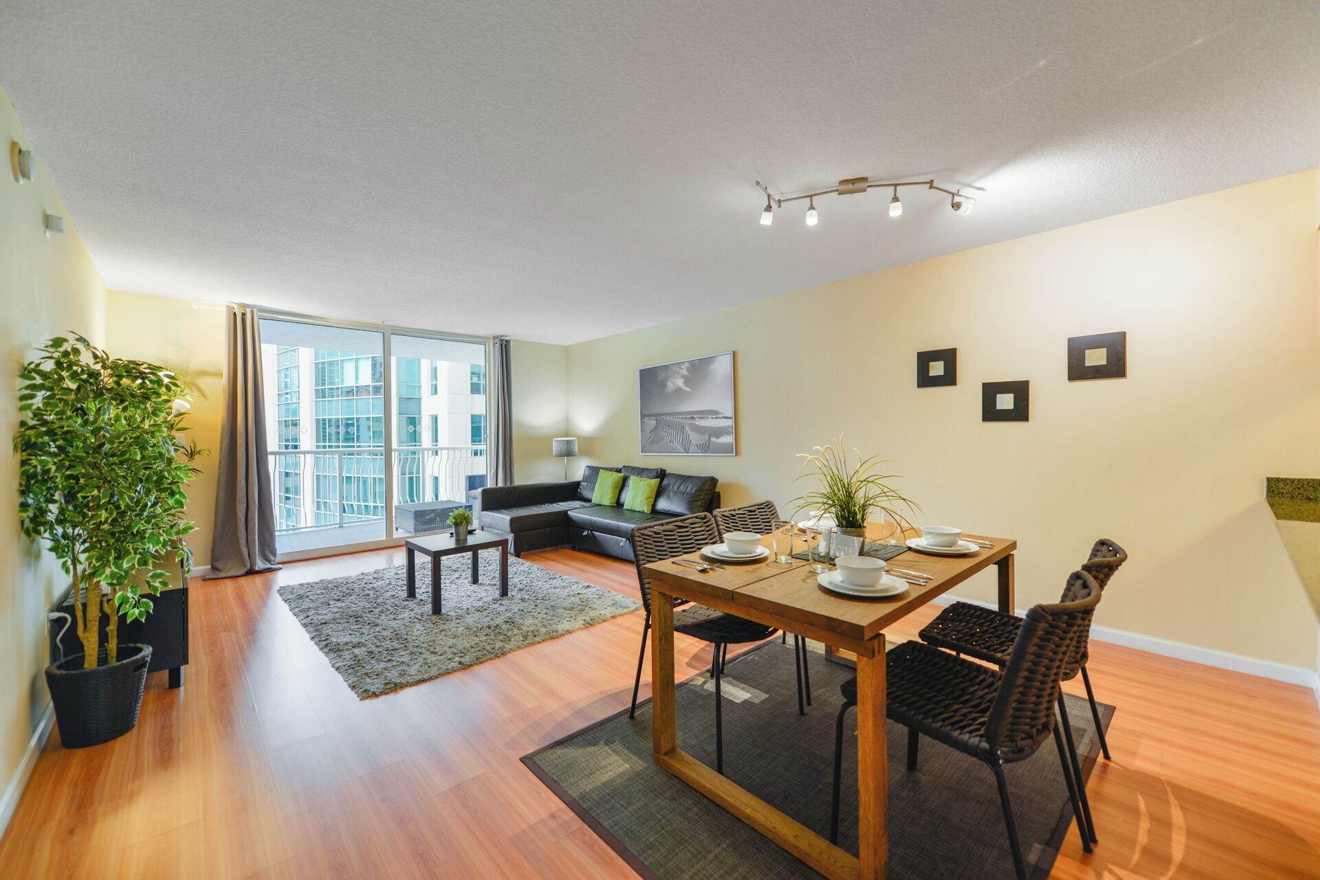 Un salon moderne comprenant un coin repas, un canapé, une table basse et une grande fenêtre donnant sur des immeubles.