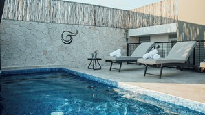 A swimming pool with lounge chairs and a stone wall with a decorative symbol. - Elegant Loft in Tulum with Pool & Gym (Tulum)