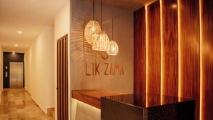 A reception area with a wooden reception desk, a wall-mounted sign, and a hanging light fixture. - Elegant Loft in Tulum with Pool & Gym (Tulum)