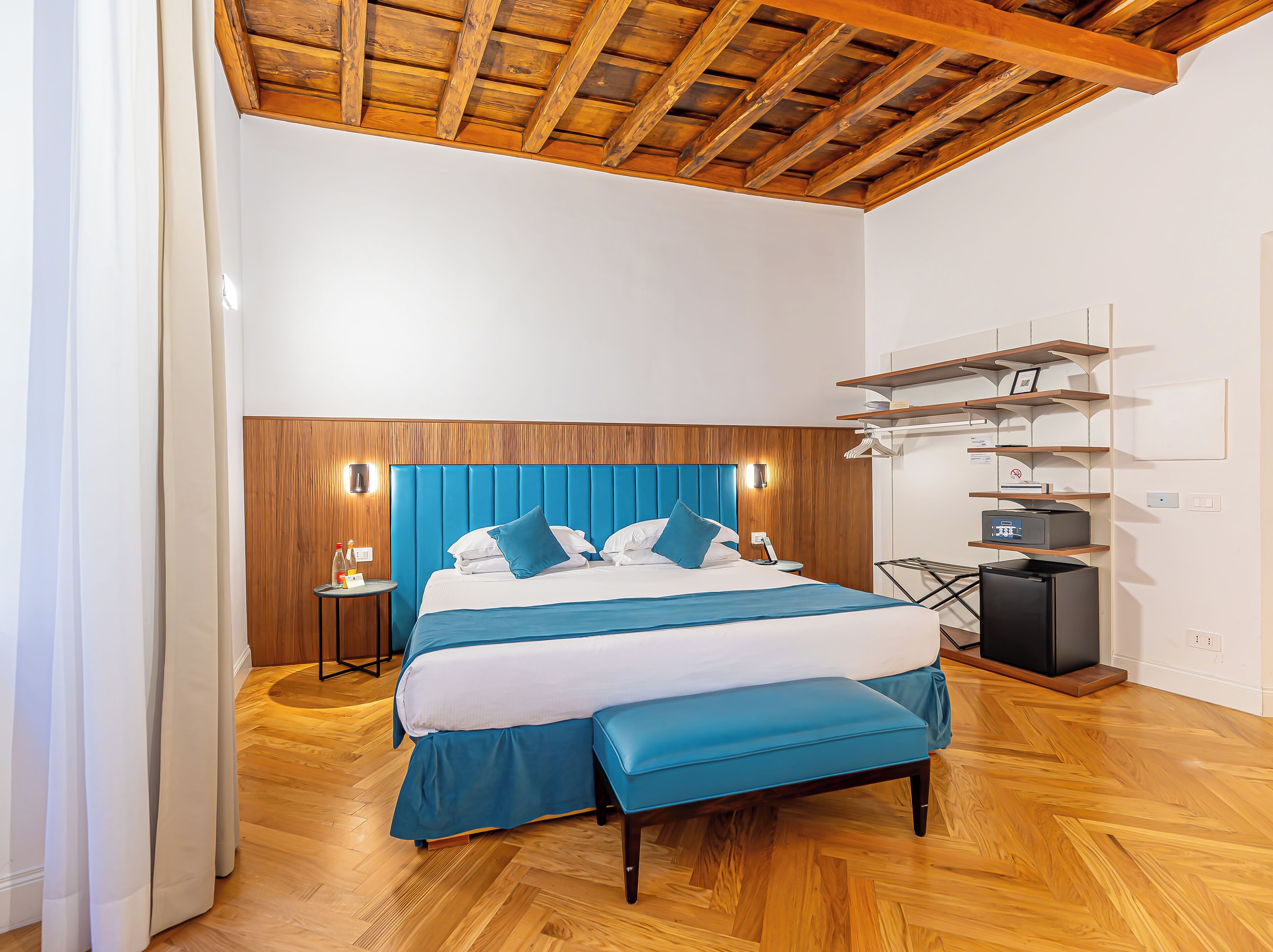 Une chambre moderne avec un plafond en bois, un grand lit avec une literie bleue, une table de chevet et un meuble pour la télévision intégré.