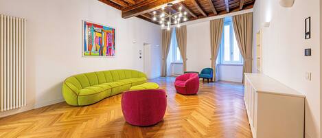 Un salon spacieux doté d’un parquet en bois disposé en point de Hongrie, d’un canapé vert, d’un pouf rouge et d’une chaise bleue.