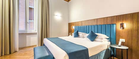 A bedroom with a wooden ceiling, a large bed with blue bedding, a bedside table, and a window with curtains.