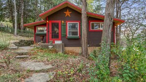 A rustic cabin with a star on the roof, surrounded by trees and a stone pathway. - Charming 1920's cottage in Afton up on bluff, river views! Swim, hike, explore! (Hastings)