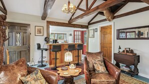 A rustic interior with exposed wooden beams, leather sofas, a wooden dining table, and a bar area. - Charming 1920's cottage in Afton up on bluff, river views! Swim, hike, explore! (Hastings)