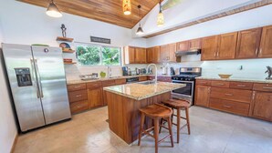 Una cocina moderna con armarios de madera, un refrigerador de acero inoxidable, una encimera de granito y una isla integrada con taburetes.
