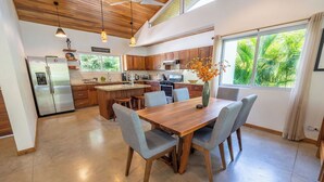 Una cocina moderna con armarios de madera, un refrigerador de acero inoxidable y un comedor con mesa y sillas de madera.