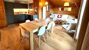A cozy cabin interior with a wooden dining table, chairs, a sofa, and a kitchen area.