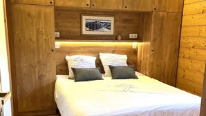 A wooden-paneled bedroom with a bed, pillows, a white rug, and a framed picture on the wall.