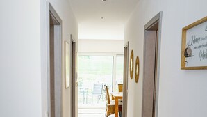 A hallway with wooden flooring, white walls, and a view to an outdoor seating area.