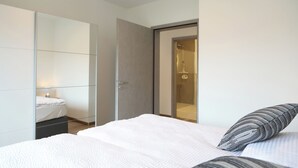 A modern bedroom with a bed, a large mirror, and a sliding door leading to a bathroom.