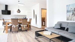 A modern living room with a grey sofa, a wooden coffee table, and a dining area with wicker chairs and a wooden table.