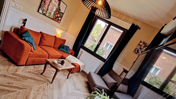 A modern living room with a herringbone floor pattern, a sofa, a coffee table, and a large window with a view of a brick building. - Between station and Seine Renovated family home. Pets welcome! (Oissel)