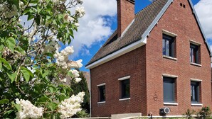 A red brick house with a sloped roof, a stone pathway leading to the entrance, and white flowering trees in the foreground. - Between station and Seine Renovated family home. Pets welcome! (Oissel)