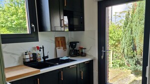 A modern kitchen with black cabinets, a microwave, a coffee maker, and a window providing a view of greenery. - Between station and Seine Renovated family home. Pets welcome! (Oissel)