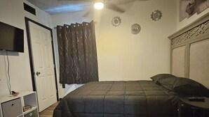 A bedroom with a bed, a ceiling fan, a TV mounted on the wall, and a door.