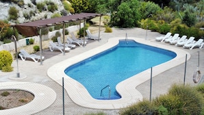 Une piscine rectangulaire dotée d’un plongeoir, entourée d’une clôture et ombragée par une pergola.