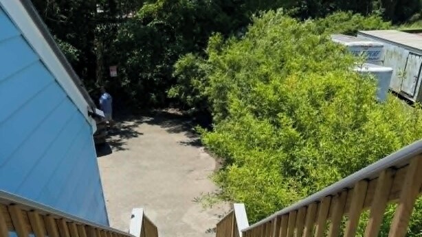 Una escalera de madera que lleva a un espacio cubierto con un edificio azul a un lado.