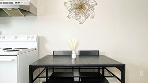 Una cocina con una estufa blanca, una mesa de comedor negra con un jarrón blanco y un adorno de pared.