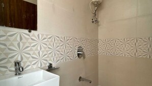 Un baño con lavamanos blanco, un espejo, ducha con cabezal de ducha manual y un inodoro con un cubo de basura de plástico.