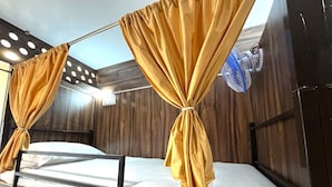Una cama litera con dos camas, cada una con una cortina. Hay un ventilador en la pared.