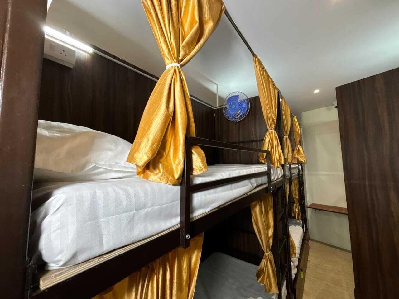 Un lit superposé avec des rideaux dorés attachés aux coins, un ventilateur de plafond et un mur en bois.