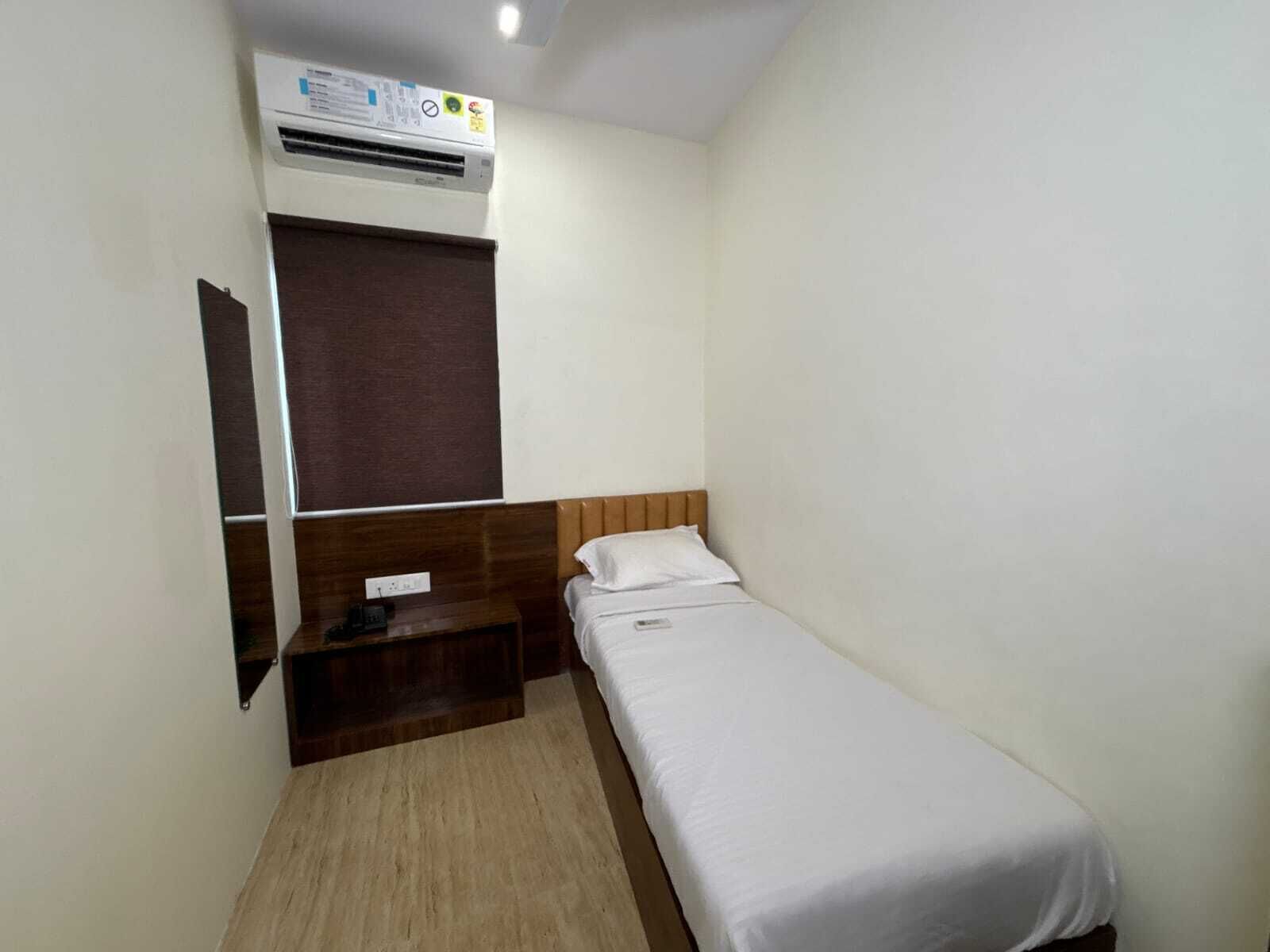 A small, single-bed room with a wooden headboard, a bedside table, and a built-in air conditioning unit.