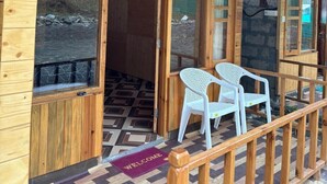 Eine Holzhütte mit überdachter Veranda, zwei weißen Plastikstühlen und einer Fußmatte.