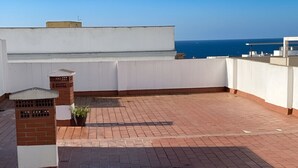 Une terrasse sur le toit, avec un sol en briques, des murs blancs et une vue sur la mer.