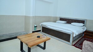 A bedroom with a bed, a wooden table, and a small trash bin. - Hotel Red Inn (Jodhpur)