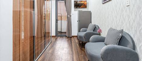 Un salon moderne avec un canapé gris, une porte vitrée donnant sur un balcon et un tableau encadré accroché au mur.