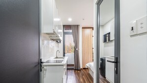 A compact kitchen with a sink, stove, and microwave, leading to a bedroom with a window and curtains. - Lalala Inn Hotel (Ho Chi Minh City)