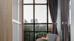 A bedroom with a large window, a round table with a vase of flowers, a sofa, and a bed. - Lalala Inn Hotel (Ho Chi Minh City)