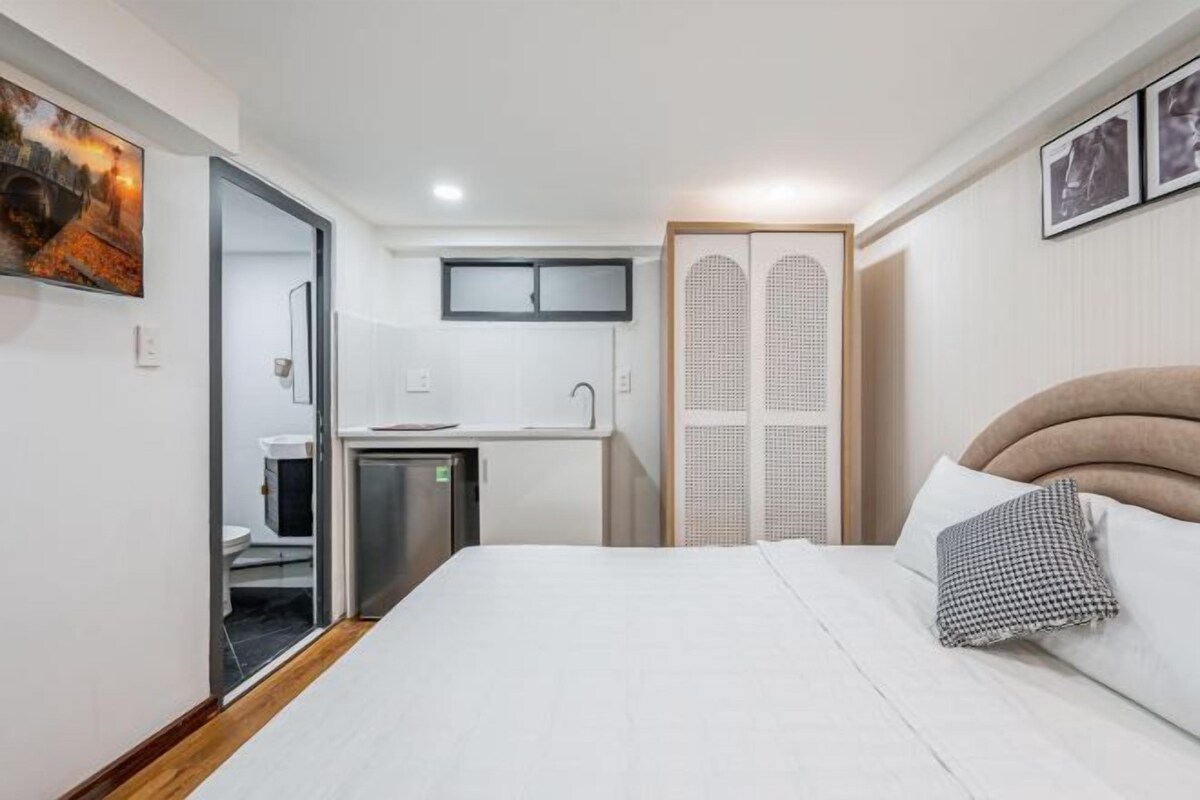 Quarto de hotel moderno com cama, kitchenette, banheiro e armário.