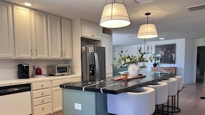A modern kitchen with white cabinets, a central island with bar stools, a refrigerator, a microwave, and a coffee maker.